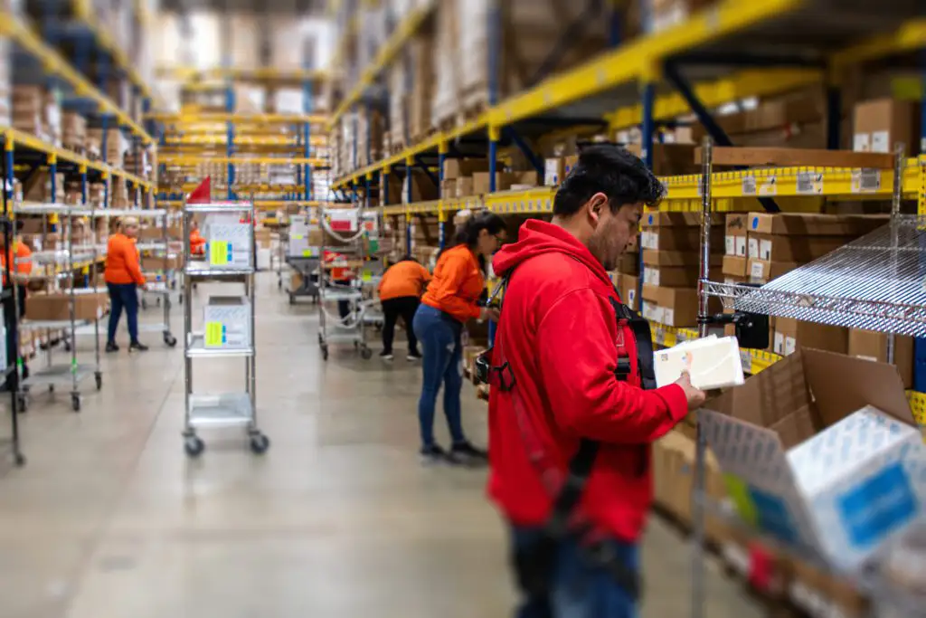 Warehouse employee picking a client's order and placing items in a box on a cart.